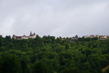 Fototapeta na wymiar Idyllisch liegendes Schloss hinter einem grünen Wald höherliegend auf einem Berg
