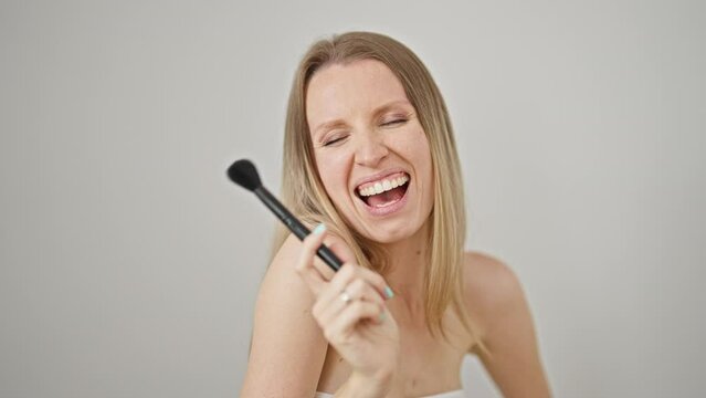 Young blonde woman smiling confident holding make up brush over isolated white background