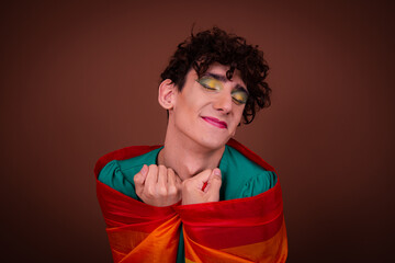 Drag queen with a rainbow flag posing in the studio and listening to music.