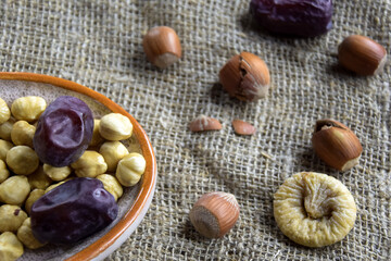 Filbert kernels, sweet dates, figs and hazelnuts in a shell on burlap background. Healthy nutrition, diet food, dried fruits and nuts. Close-up. Shallow depth of field. Selective focus.