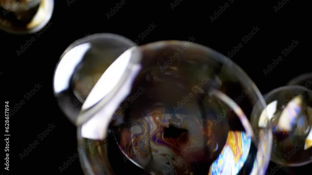 Poster colorful soap bubbles fly in an empty space on isolated black background. many large, small rainbow 
