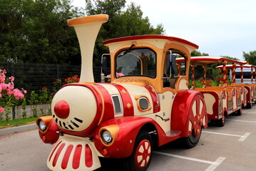 Excursion electric train for park walk . A small train ride for children stands in a parking lot in the park.