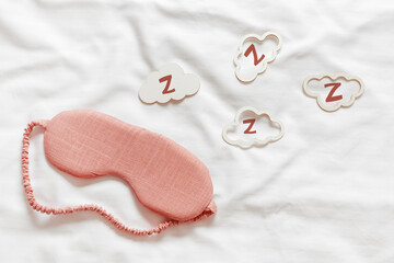 Above view pink sleep mask and clouds shapes with zzz snore sounds on white wavy cloth background. Eye cover mask for best sleep. Concept dream well, comfort rest at night. Minimal Aesthetic