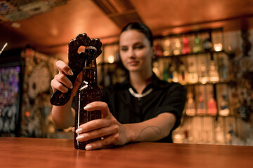 Close up of a female bartender opening a closed glass bottle of beer on the bar in a club bar