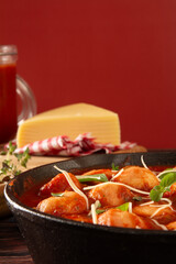 Delicious Gnocchi with Red tomato Sauce and Basil served in a black skillet pan in a red background with parmesan cheese in front view