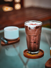 a glass of cold ice blended chocolate served with whipped cream and chocolate ground, on a table at a cafe