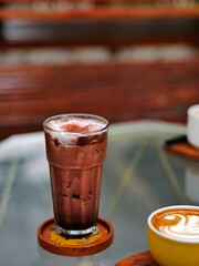 a glass of cold ice blended chocolate served with whipped cream and chocolate ground, on a table at a cafe