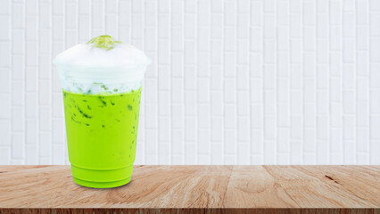 Iced matcha green tea latte frappuccino with milk foam in takeaway cup on wooden table, Summer...