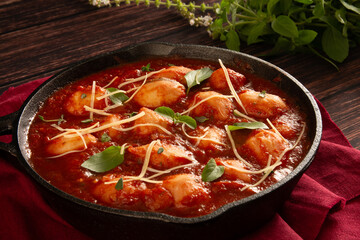 Delicious Gnocchi with Red tomato Sauce and Basil served in a black skillet pan in a wooden background in front view