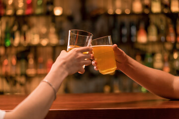 Close up of a couple of guys and a girl toast with glasses of beer at the bar in a club bar 