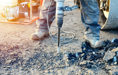 Builder breaking asphalt with electric breaker