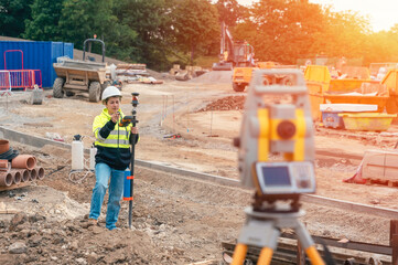 Female site engineer surveyor working with theodolite total station EDM equipment on a building construction site outdoors