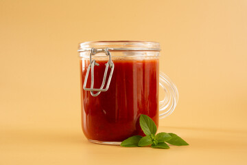 Fresh Tomato Sauce in a Glass Jar with basil leaves, sliced tomatoes in a beige background in front view