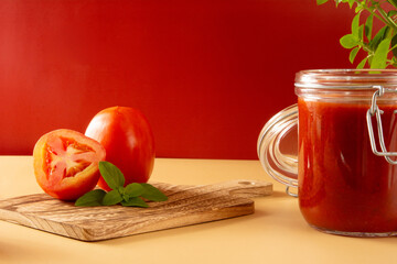 Fresh Tomato Sauce in a Glass Jar with basil leaves, sliced tomatoes in a red background in front view