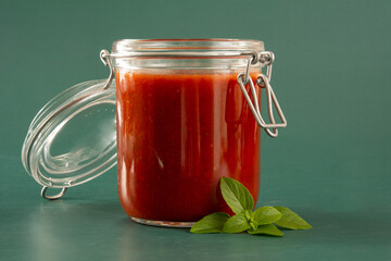 Fresh Tomato Sauce in a Glass Jar with basil leaves, sliced tomatoes in a green background in front view