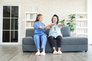 Asian elderly senior woman try to stretch her arms with support from lovely nurse about wrist injury at nursing home sofa. Cute asian caregiver helping senior woman physical therapy.