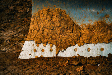 The shiny steel blade of a bulldozer caked with mud sits in brown dirt