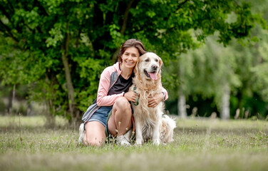 Pretty girl with golden retriever dog sitting at nature. Beautiful young woman hugging purebred pet doggy labrador in park at summer