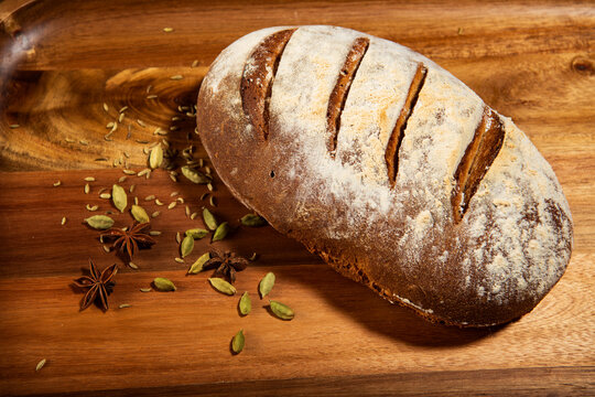 A fresh loaf of homemade rye bread with cardamom pods on a wood cutting board