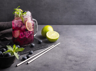 Refreshing blueberry mojito or lemonade with lime, mint and ice on a dark background with metal tube. Healthy drink made from fruits and berries.