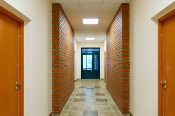 Decorative brick on the corridor wall in an office building. A black glass door at the end of the corridor of the business center. Interior design in the Art Nouveau style.