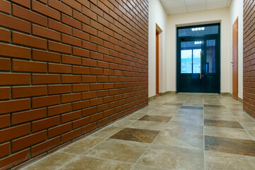 Decorative brick on the corridor wall in an office building. A black glass door at the end of the corridor of the business center. Interior design in the Art Nouveau style.