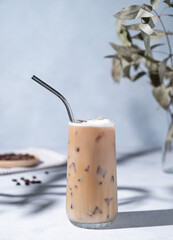 Iced coffee latte in a tall glass with milk on a light background with coffee beans, branch and...