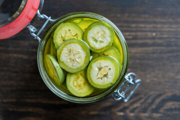 Sliced unripe walnuts in alcohol in a jar, to prepare homemade tincture, closeup. Tincture of green walnuts in a glass jar on a wooden table, top view