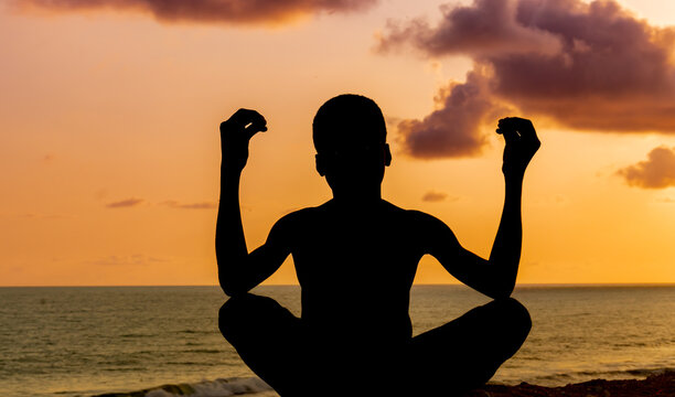 A serene image of a young boy, his silhouette poised in a yoga pose against the backdrop of a stunning ocean sunset during the solstice.