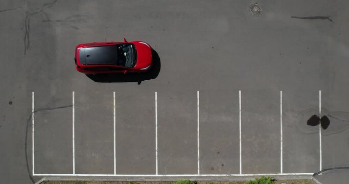 A red car drives backwards into a parking space. Car parking, aerial shot. The car is parked, top view. Empty parking