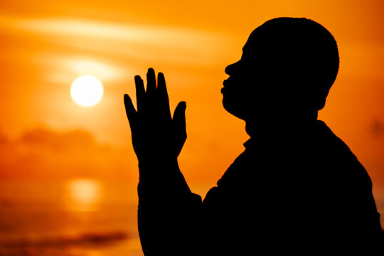 An inspiring image of a Christian worshipper, his silhouette illuminated against the beautiful solstice sky, his outstretched hands a visual representation of his deep connection with Jesus.