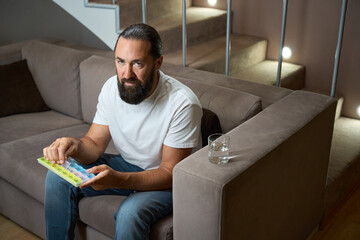 Man in casual clothes holds a pill box with medicines