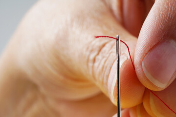 two fingers, one needle and a red thread