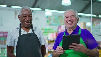 Joyful diverse Brazilian senior staff workers of supermarket chain smiling at camera with table and...