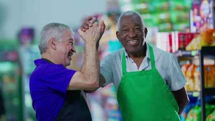 Happy diverse senior employees celebrating success with high-five standing in supermarket aisle....