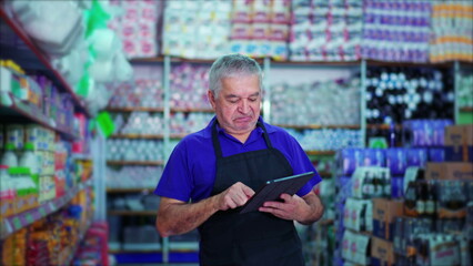 Happy Male Caucasian Senior Manager of Grocery Store Using Tablet Device to Inspect Product Inventory on Supermarket Shelf
