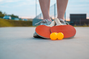 Ping pong paddle and balls on a grey background on woman's feets in sport's shoes. Close up....