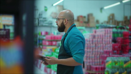 Male Grocery Store Employee with Apron Browsing Inventory on Tablet