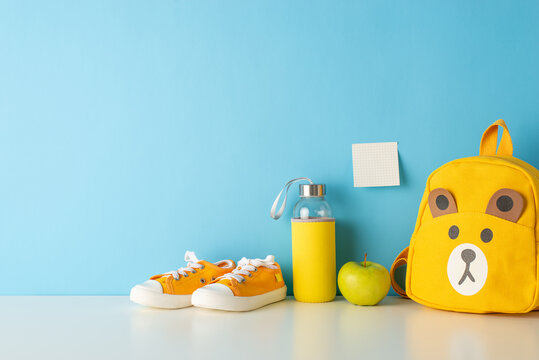 Classroom essentials on display: side view photo of desk adorned with school supplies, pencil holders, colorful pens, rulers, books, sticky notes, plasticine, and apples against a blue wall backdrop