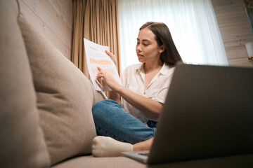 Fototapeta premium Busy young female checking documents sitting at home