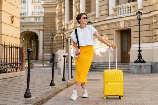 stylish woman traveling with yellow suitcase in Europe