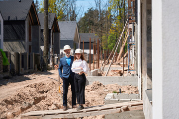 Woman general designer and foreman in hardhats standing near builded house