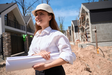 Woman general architect in hardhat coming to construction site with blueprints