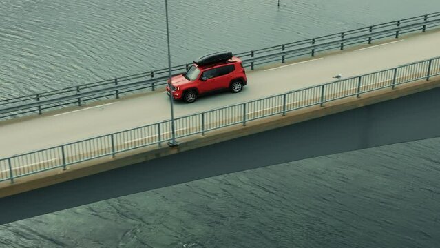 Close-up of red SUV car driving down the bridge and the road in green nordic scenery