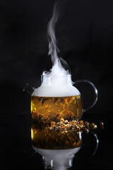 Glass teapot with hot tea on black background. Vertical photo.