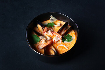 Spicy Thai Tom yam soup with shrimp and mussels in a black bowl. Mussels in the sink. Copy space.