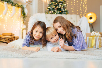 two girls and a little boy lie on the floor in a room with Christmas decor.