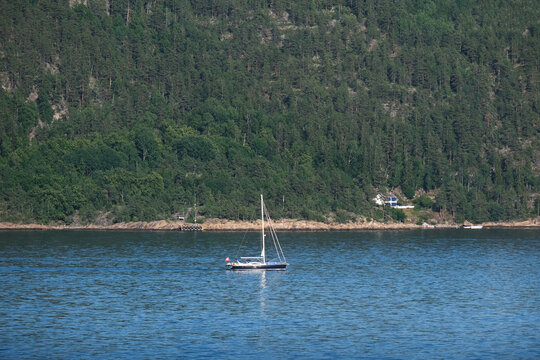 Wundersch&ouml;nes, sp&auml;rlich besiedeltes Norwegen: Segelboot f&auml;hrt langsam durch den ruhigen Oslofjord an dicht bewachsenen H&auml;ngen vorbei