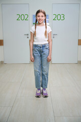 Smiling girl with pigtails stands in a hospital corridor
