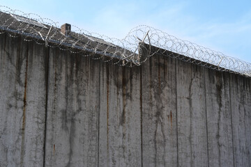 high concrete fence, barbed wire fence on top, pre-trial detention cell, building for execution of...